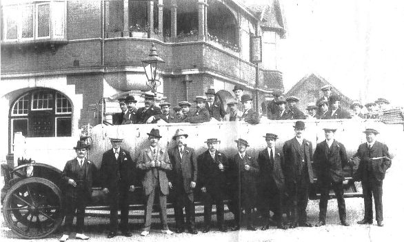 30 men and driver sitting in or standing beside a charabanc