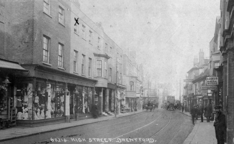 View of northern side of High Street, composed of 3-storey buildings with ground floor shops, limited view of the southern side