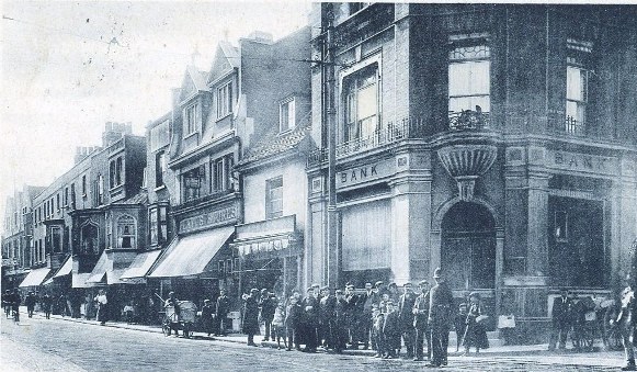 View of High Street with a crowd of people and policeman on street corner