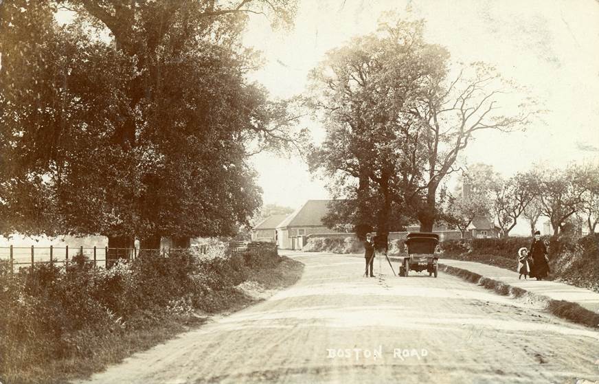 Wide country lane, farm in background, plus a photographer and his car and an older lady and small girl walking