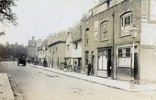 Sepia view of quiet road with miscellany of cottages on one side, horse and cart and few pedestrians