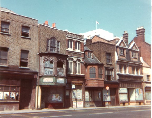 Row of dilapidated thee-storey shops, two with ornate, projecting first floor bay windows