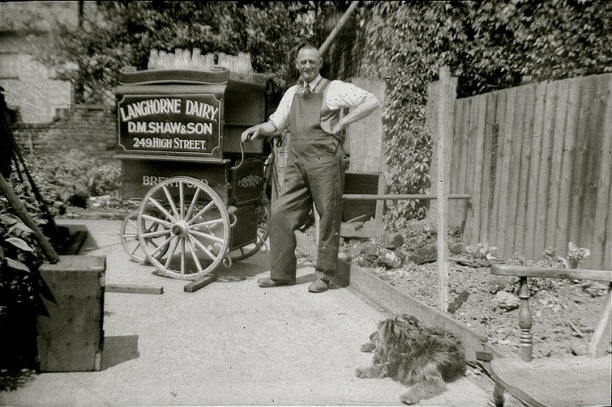 Dairyman and handcart with empty milk bottles, in back garden