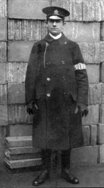 Man in doublebreasted coat, cap with badge, armband