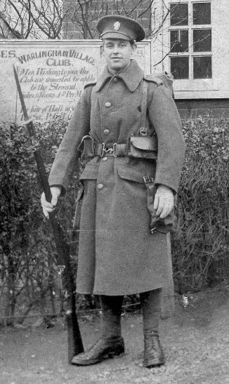 Young soldier carrying rifle and bayonet, standing outside Warlingham Village Club