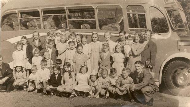 Sepia photo of 1940s coach with around 30 children, all ages, and a handful of adults