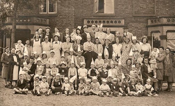 Sepia photo of group of over 70 people outside brick built property