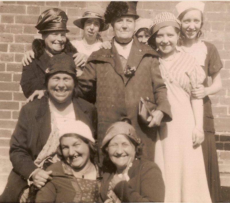 Photo taken outside, nine ladies dressed up, all smiles, all in hats, seven aged 40+ and two younger
