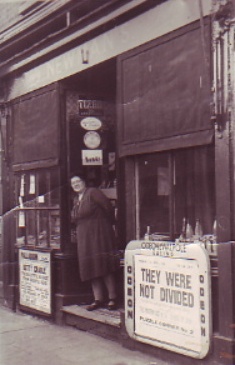 B/w photo of  Alice Newman, shopkeeper, standing in the entrance to her novelties shop