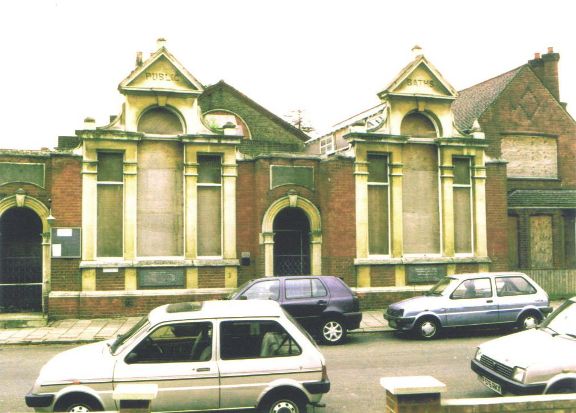 Boarded up red brick building with two pediments inscribed 'Public' and 'Baths'