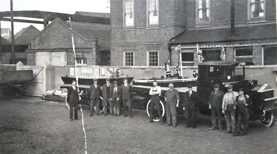 Lorry with two boats loaded, men stand in front posed for photo